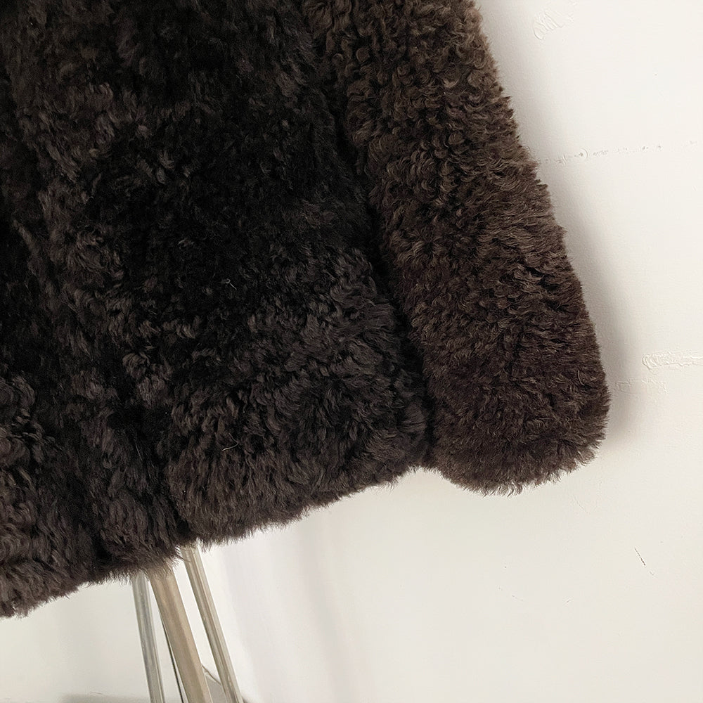 Close-up of premium curly 100% real lamb wool shearling texture in dark chocolate