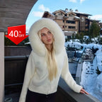 Woman wearing a white luxury knitted hoodie with a massive white real fox fur hood trim in a luxury bathroom setting